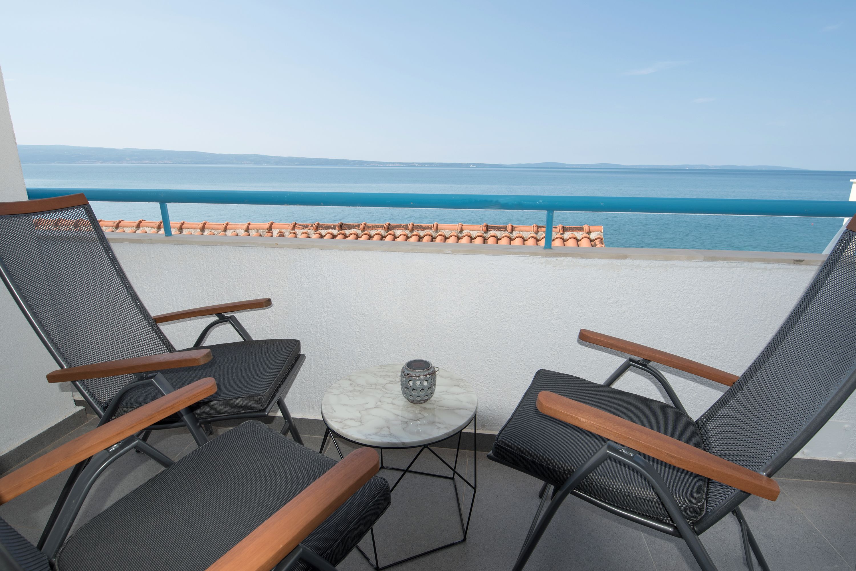 A balcony with two chairs and a small table, overlooking a coastal view.