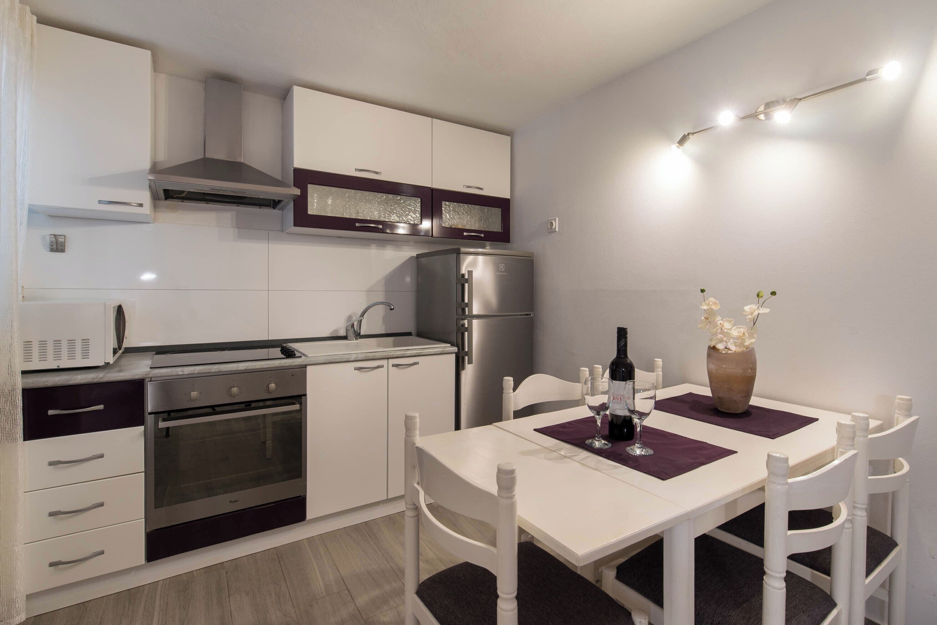 Una cocina moderna con armarios blancos, horno empotrado y refrigerador de acero inoxidable.