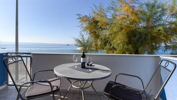 A balcony with a round table and two chairs, overlooking a body of water and a tree.