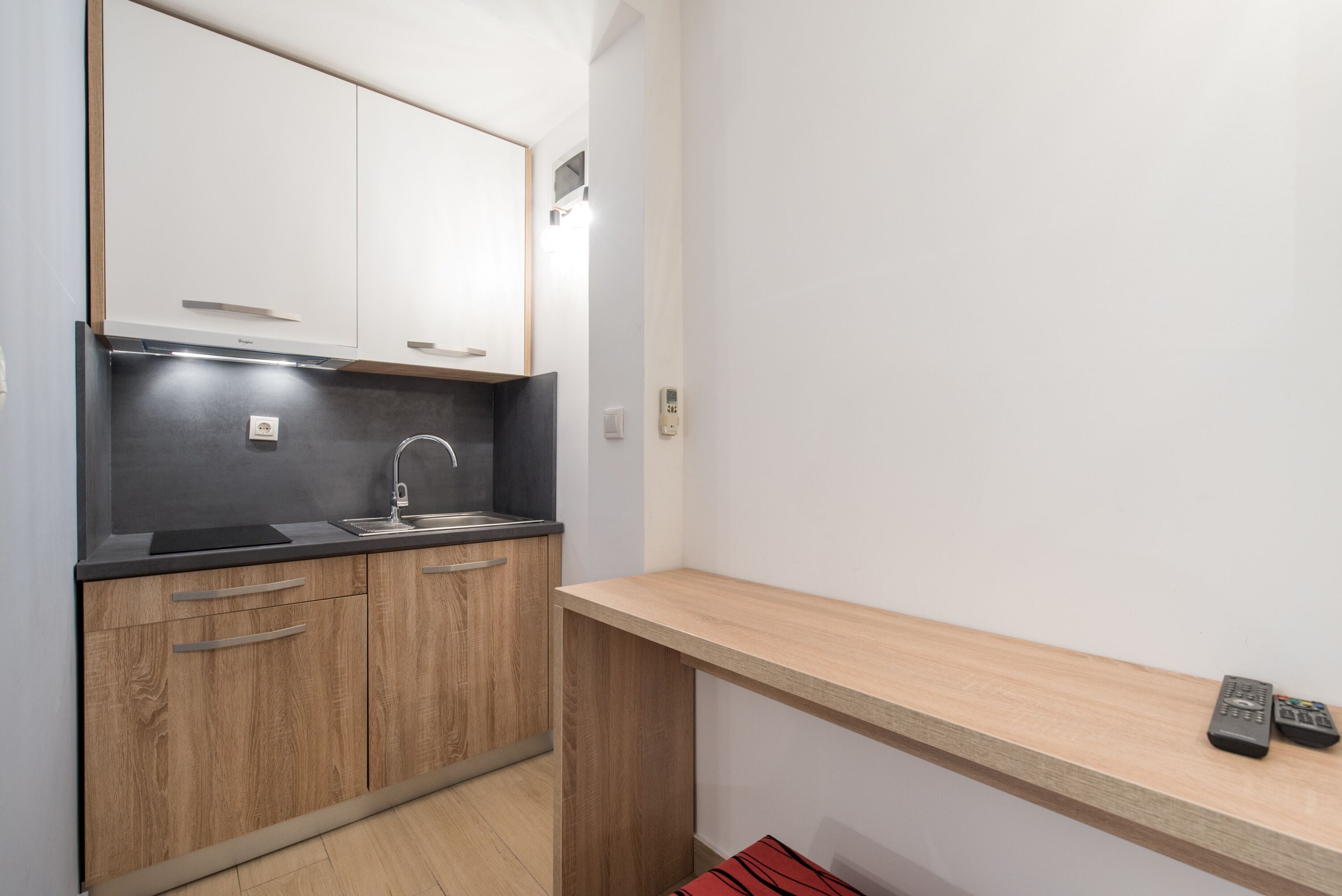 Una cocina compacta con armarios de madera, una encimera negra y un microondas integrado.