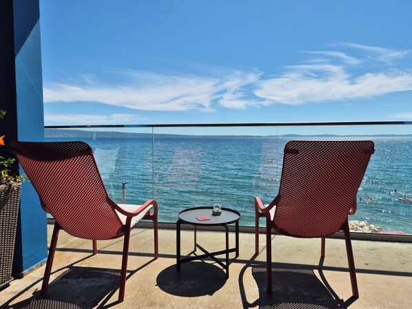 Varanda com duas cadeiras de malha vermelha e uma pequena mesa redonda, com vista para um mar calmo e terra distante.