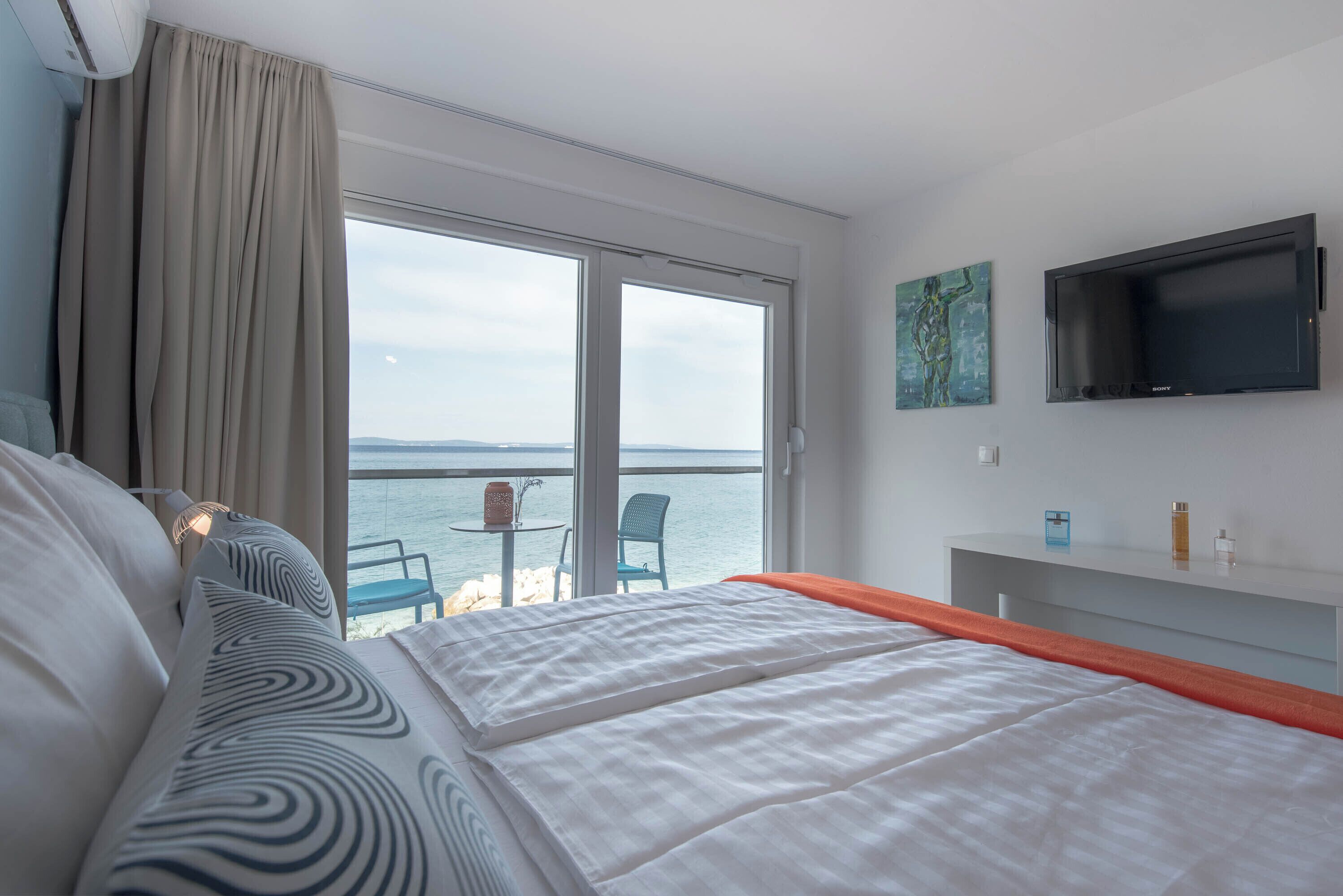 A hotel room with a bed, a TV, a balcony with a table and chairs, and a view of the sea.