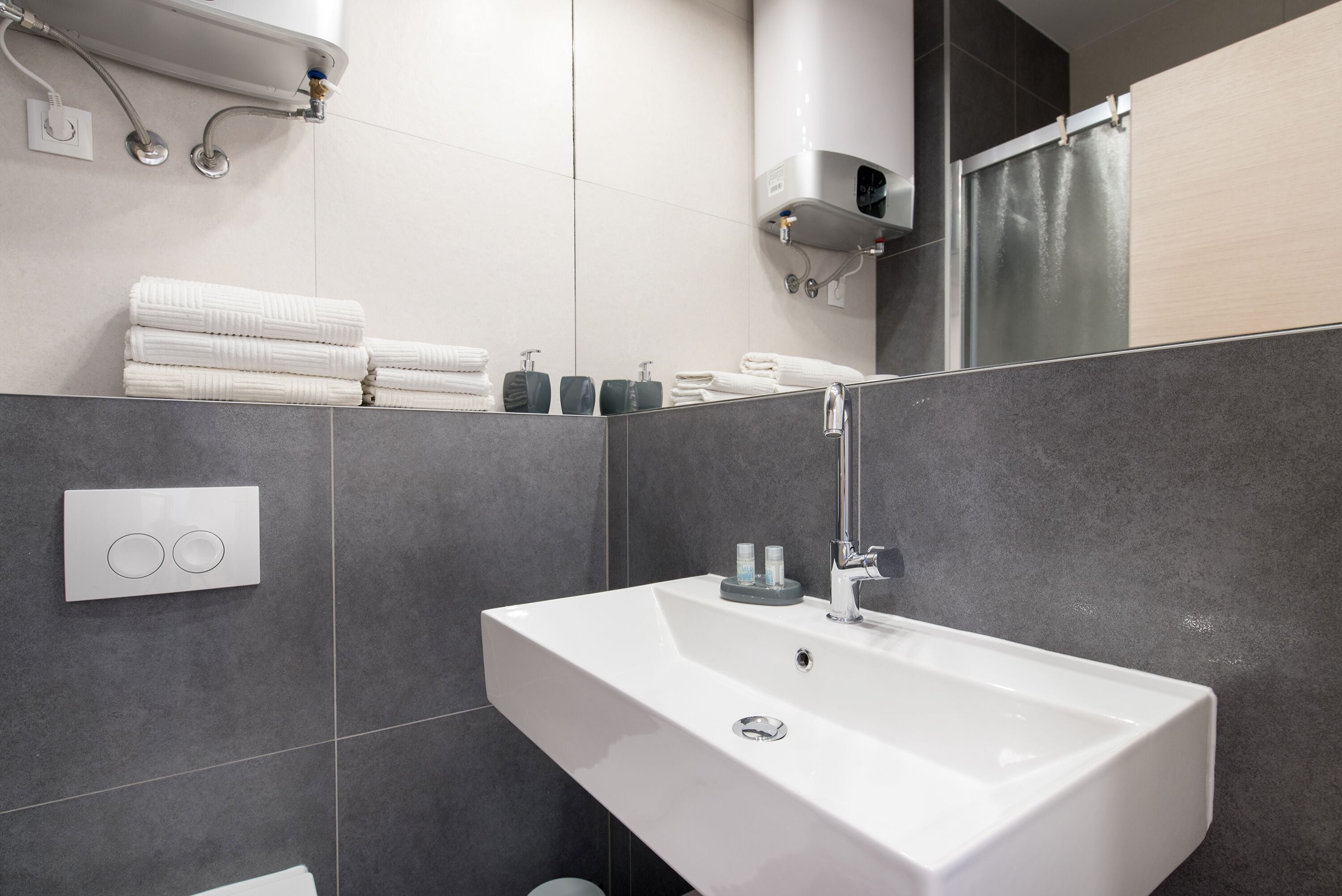 Un bagno moderno con un lavandino bianco, piastrelle grigie e un porta asciugamani con asciugamani piegati.