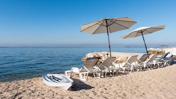 A beach with lounge chairs and umbrellas, a boat, and a rocky shoreline.