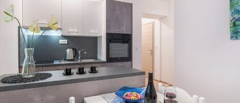 A modern kitchen with a central island, a dining table with chairs, and a bottle of wine on the table.