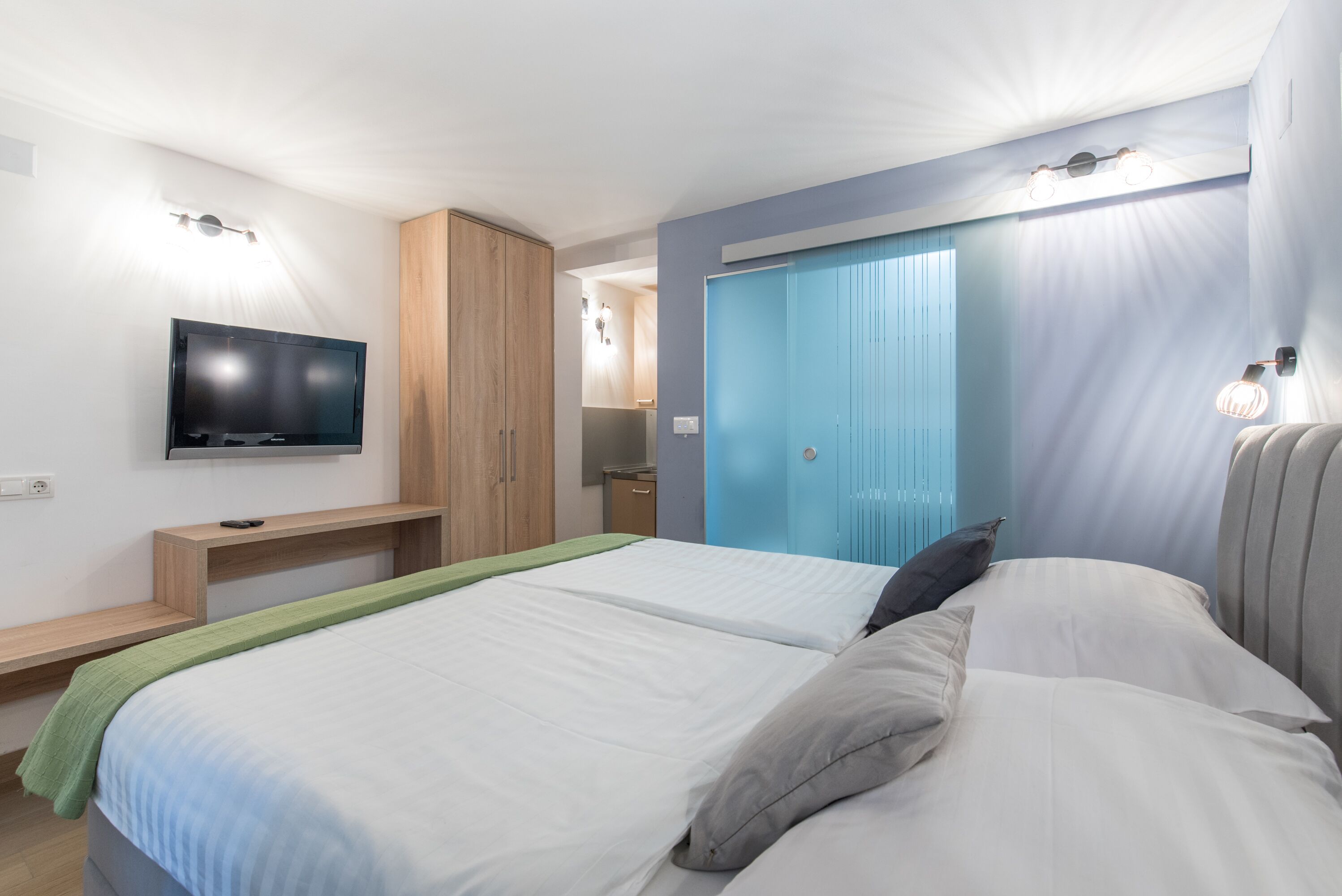 Un dormitorio con dos camas, televisión, armario y baño visible a través de una puerta abierta.