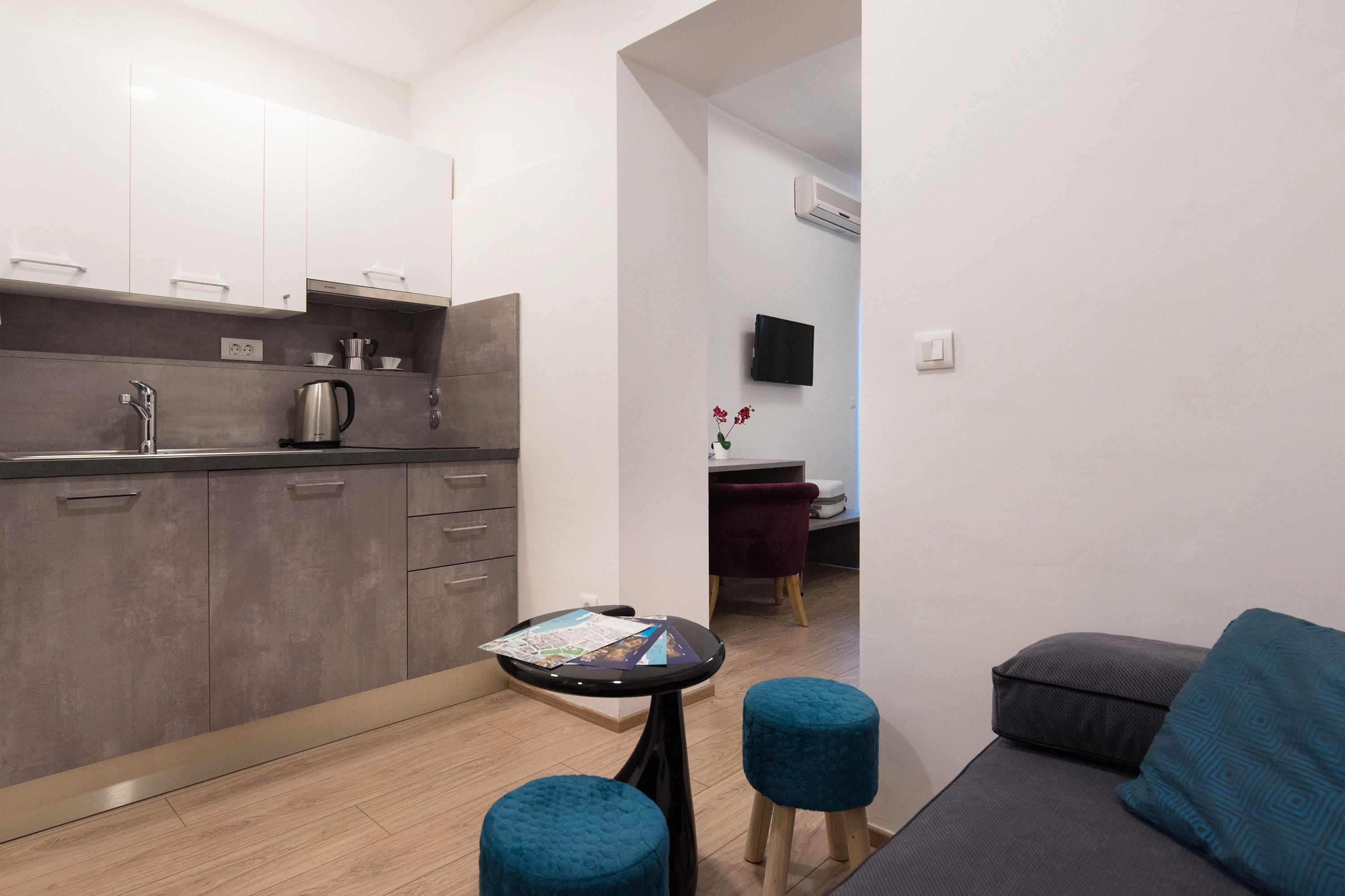 Un espacio habitable compacto con kitchenette, comedor y zona de estar con sofá y otomanas.