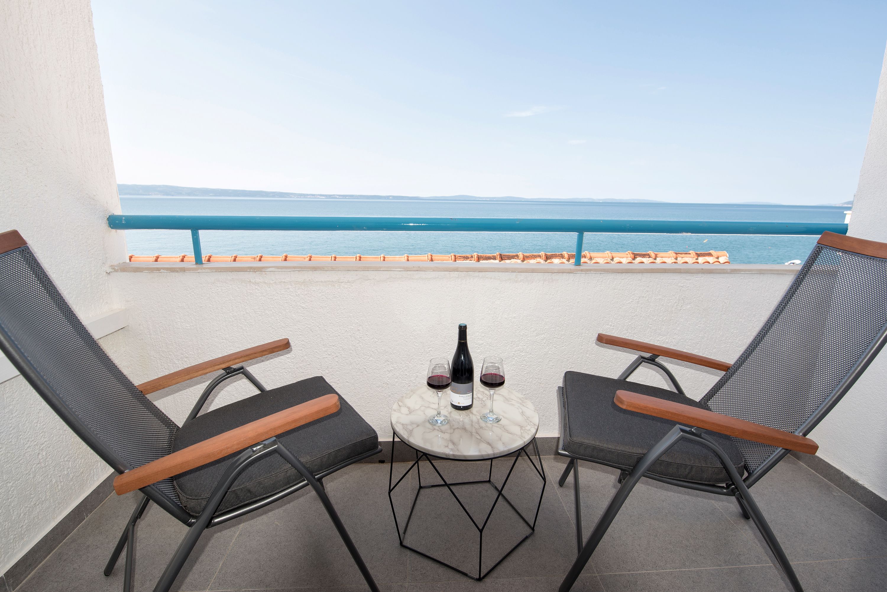 Een balkon met twee stoelen en een kleine tafel, een fles wijn en twee glazen op de tafel.