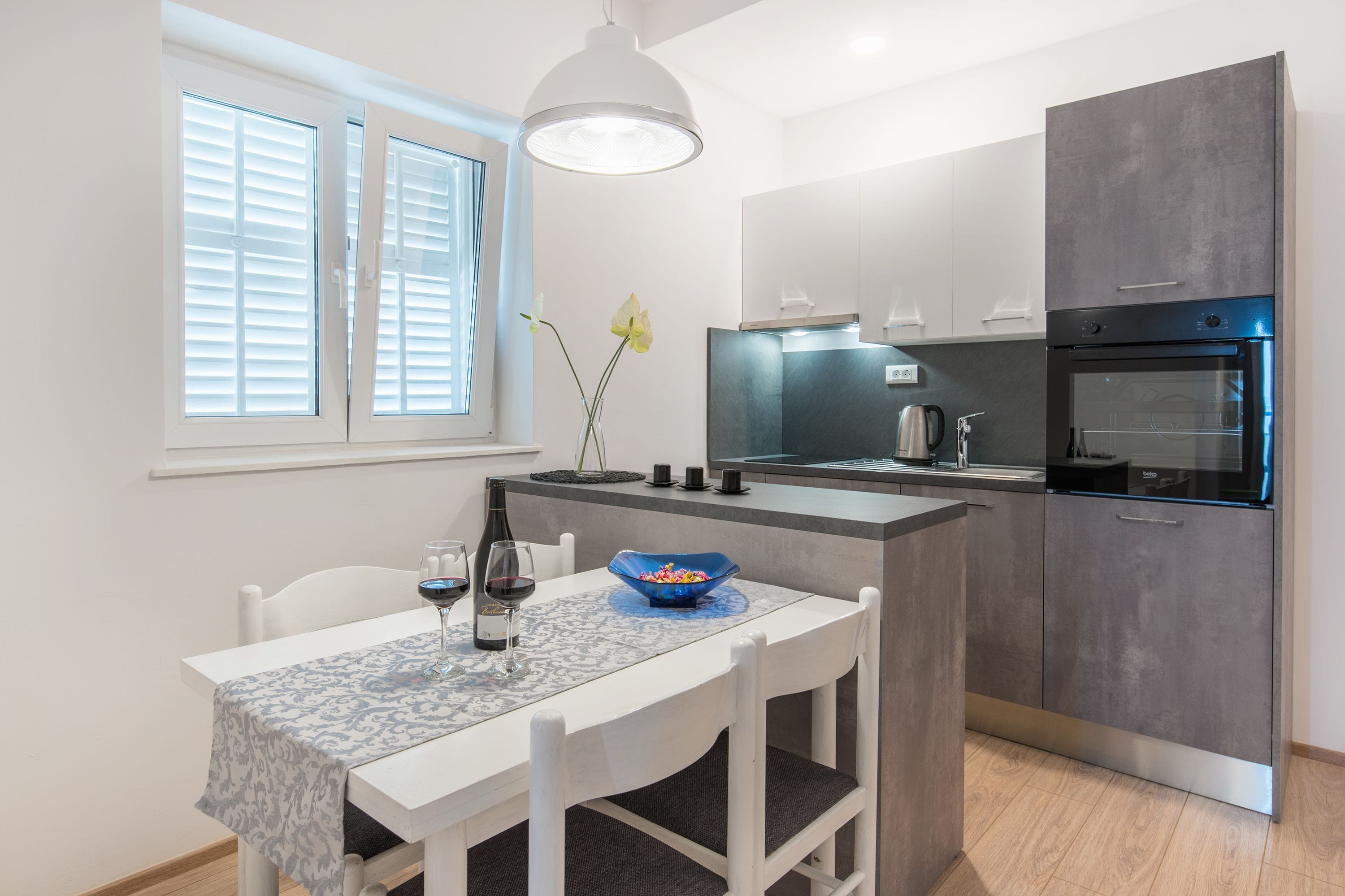 A modern kitchen with a dining area, featuring a white table, chairs, and a blue bowl.
