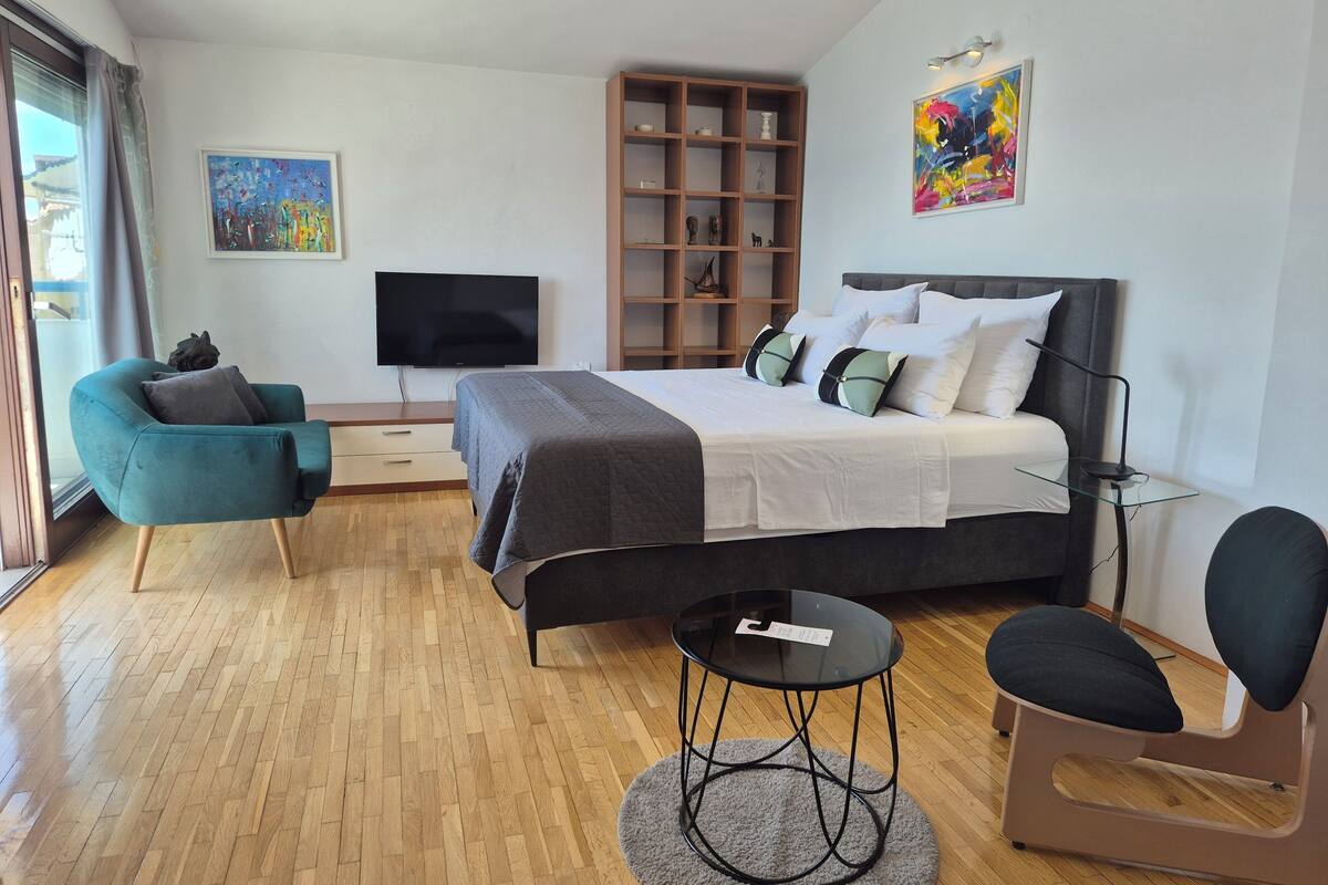 A modern bedroom with a bed, a TV, a bookshelf, a chair, and a small table.