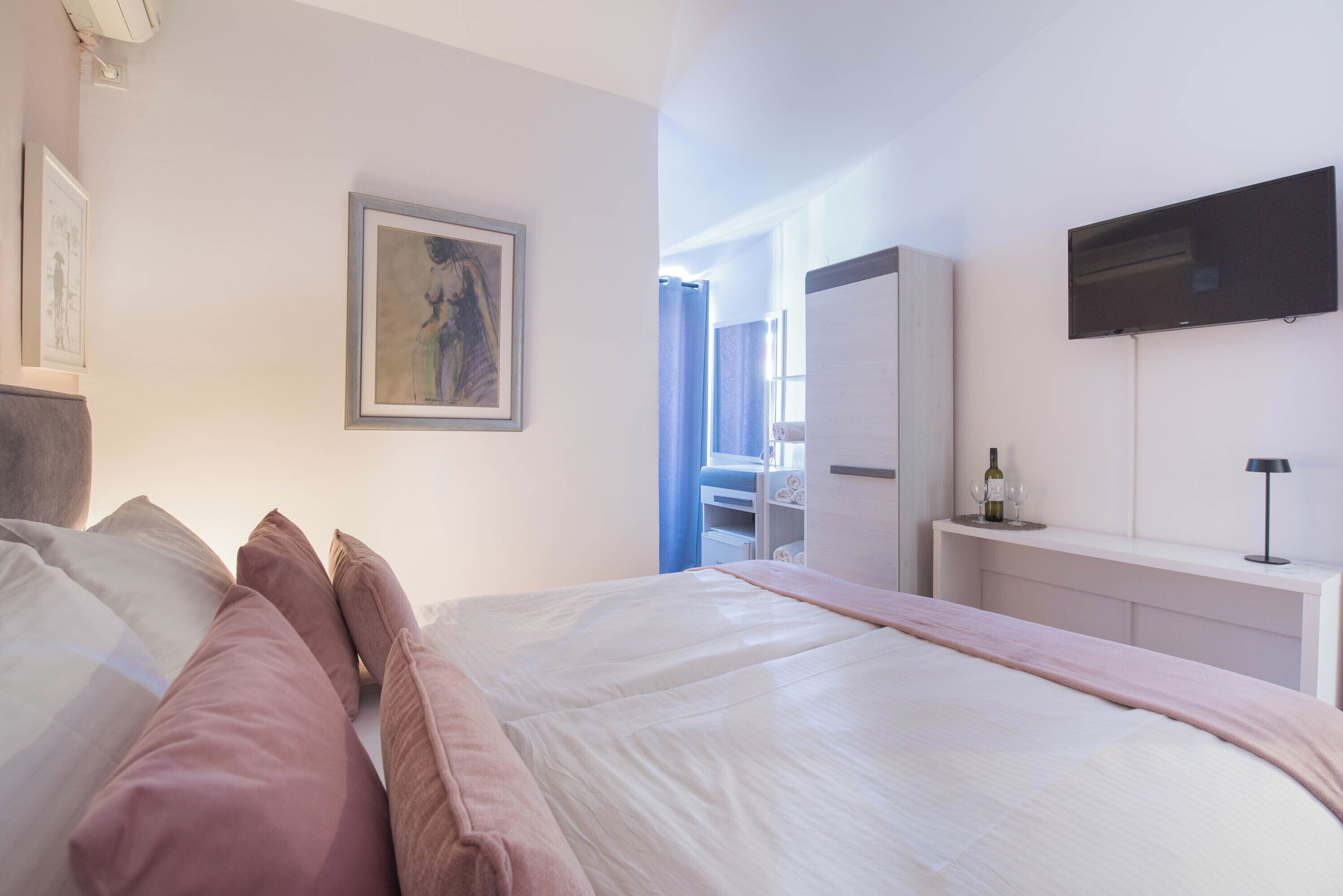 Een slaapkamer met een bed, kussens, een televisie, een kledingkast en een raam met gordijnen.