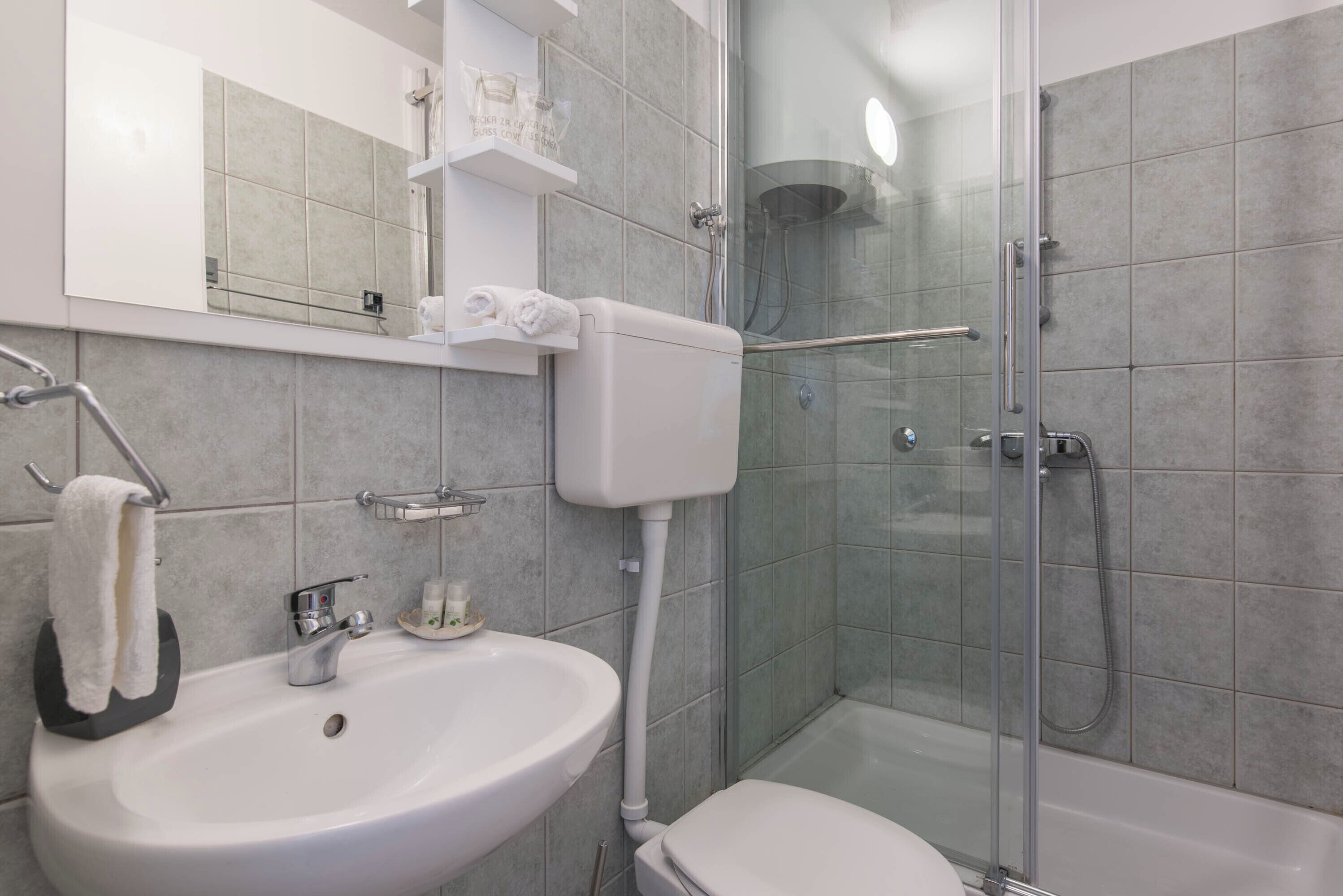 Un baño moderno con ducha de vidrio, lavamanos blanco y retrete.