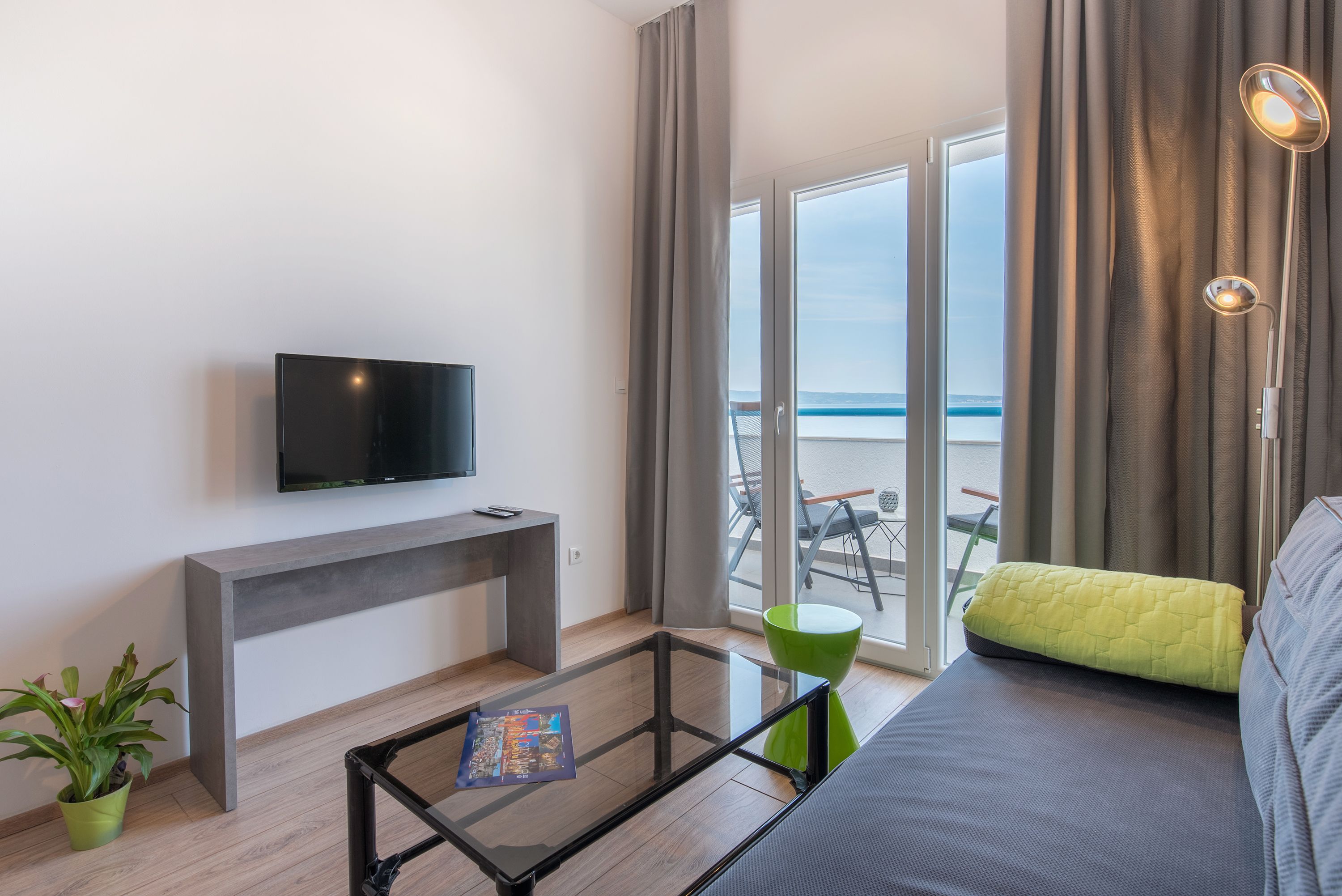Una sala de estar moderna con un televisor de pantalla plana, una mesa de centro de vidrio, un sofá y vistas al mar a través de amplios ventanales.