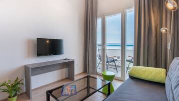 Una sala de estar moderna con un televisor de pantalla plana, una mesa de centro de vidrio, un sofá y vistas al mar a través de amplios ventanales.