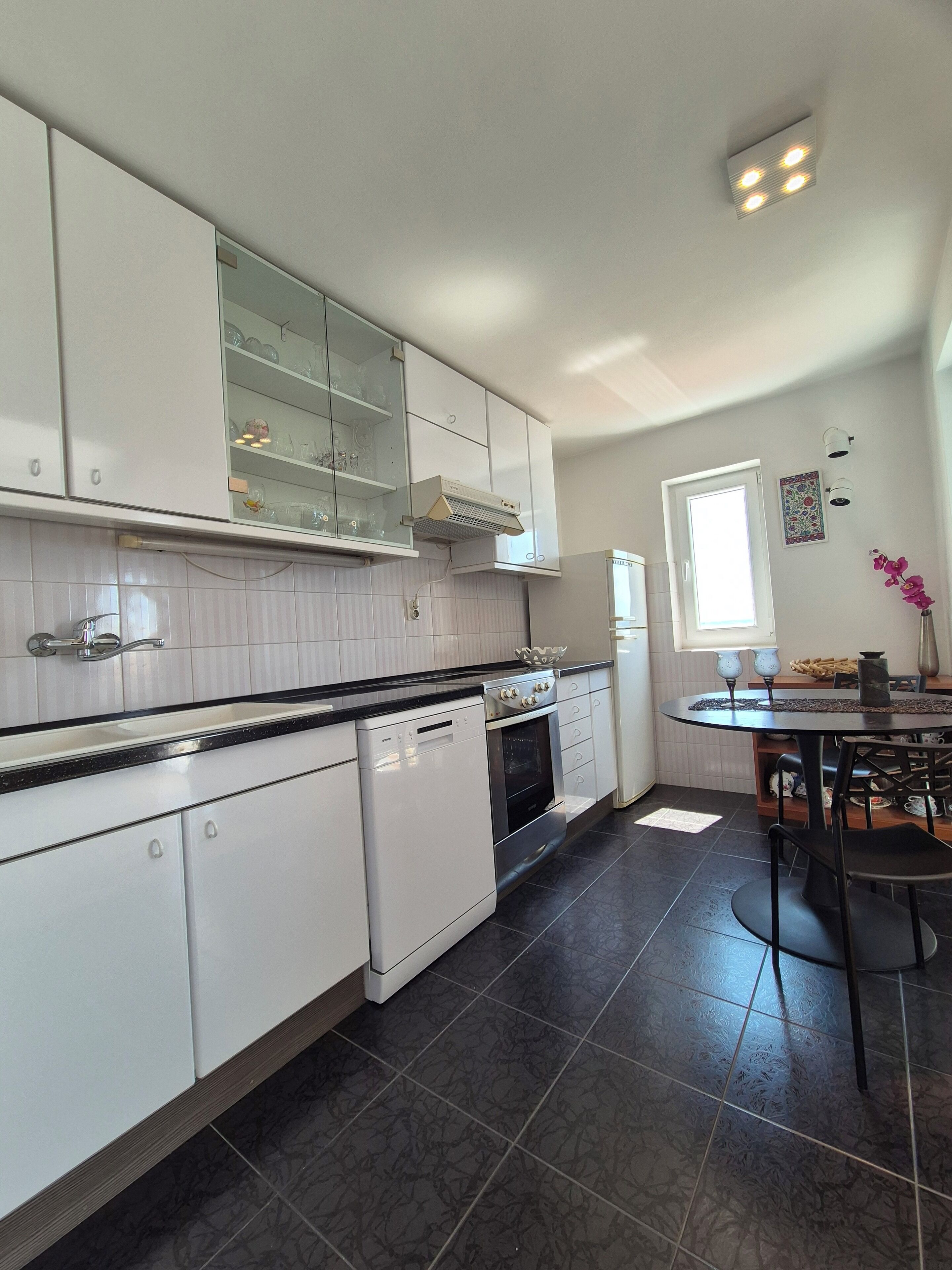 A modern kitchen with white cabinets, a black countertop, and a dining area with a table and chairs.