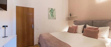 Une chambre à coucher avec un lit, une porte en bois, un téléviseur fixé au mur et un tableau.