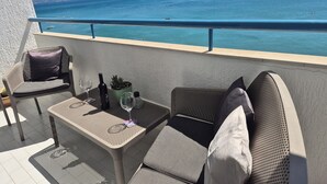 En balkon med et bord, stole, en lille plantekasse og en flaske vin.