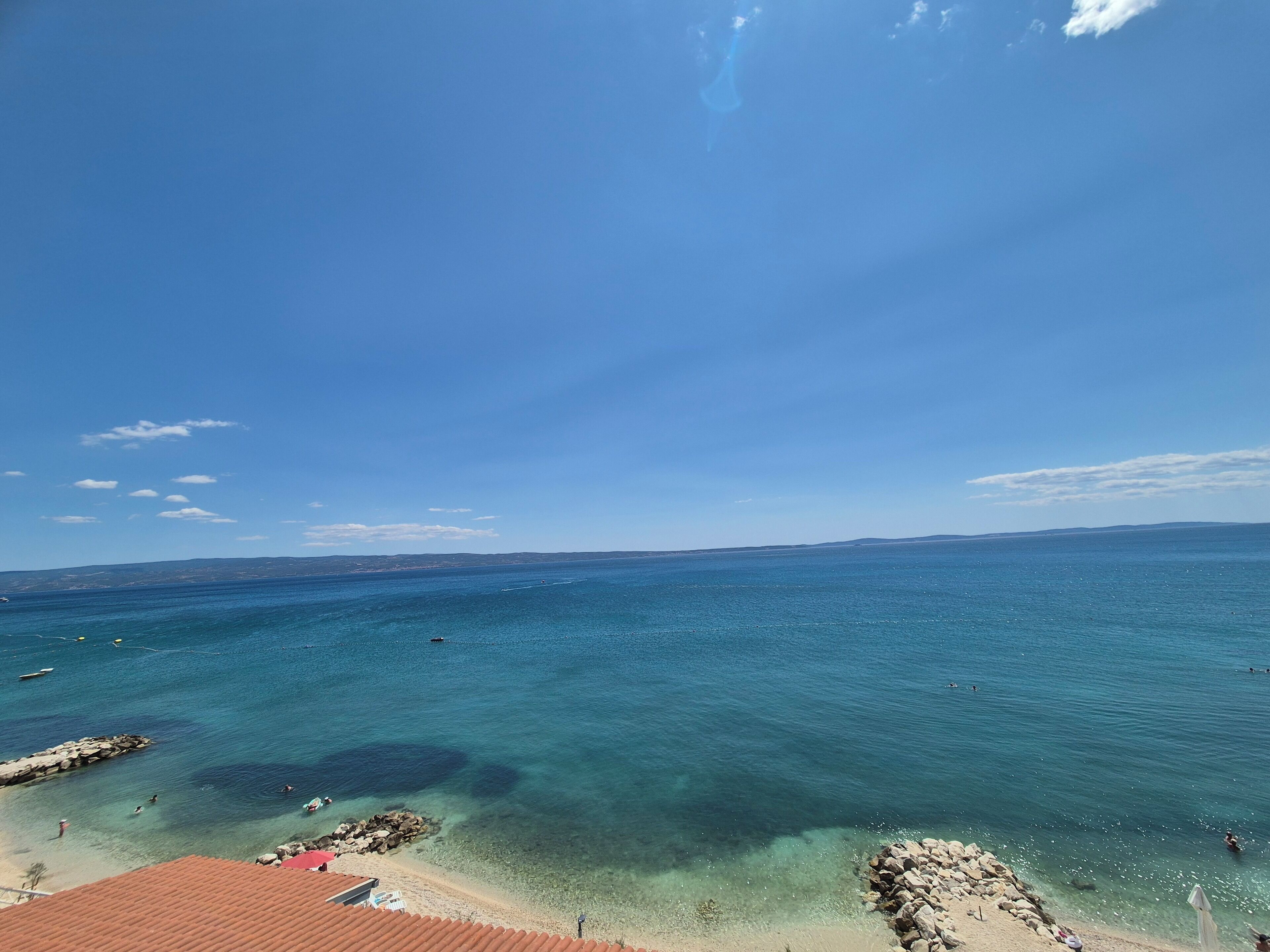 A coastal view with clear blue water, rocky shoreline, and distant land.