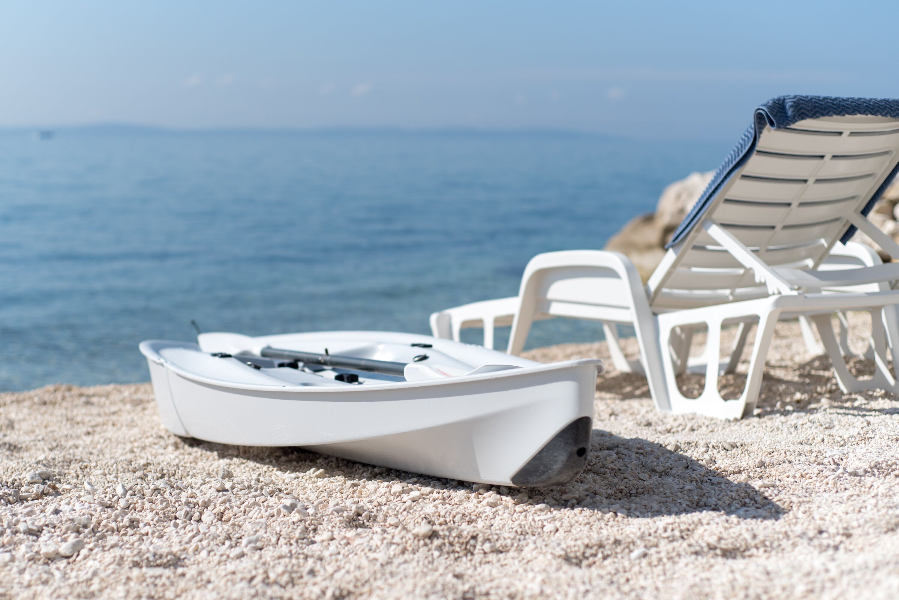 A boat on a sandy beach with a chair and a towel.