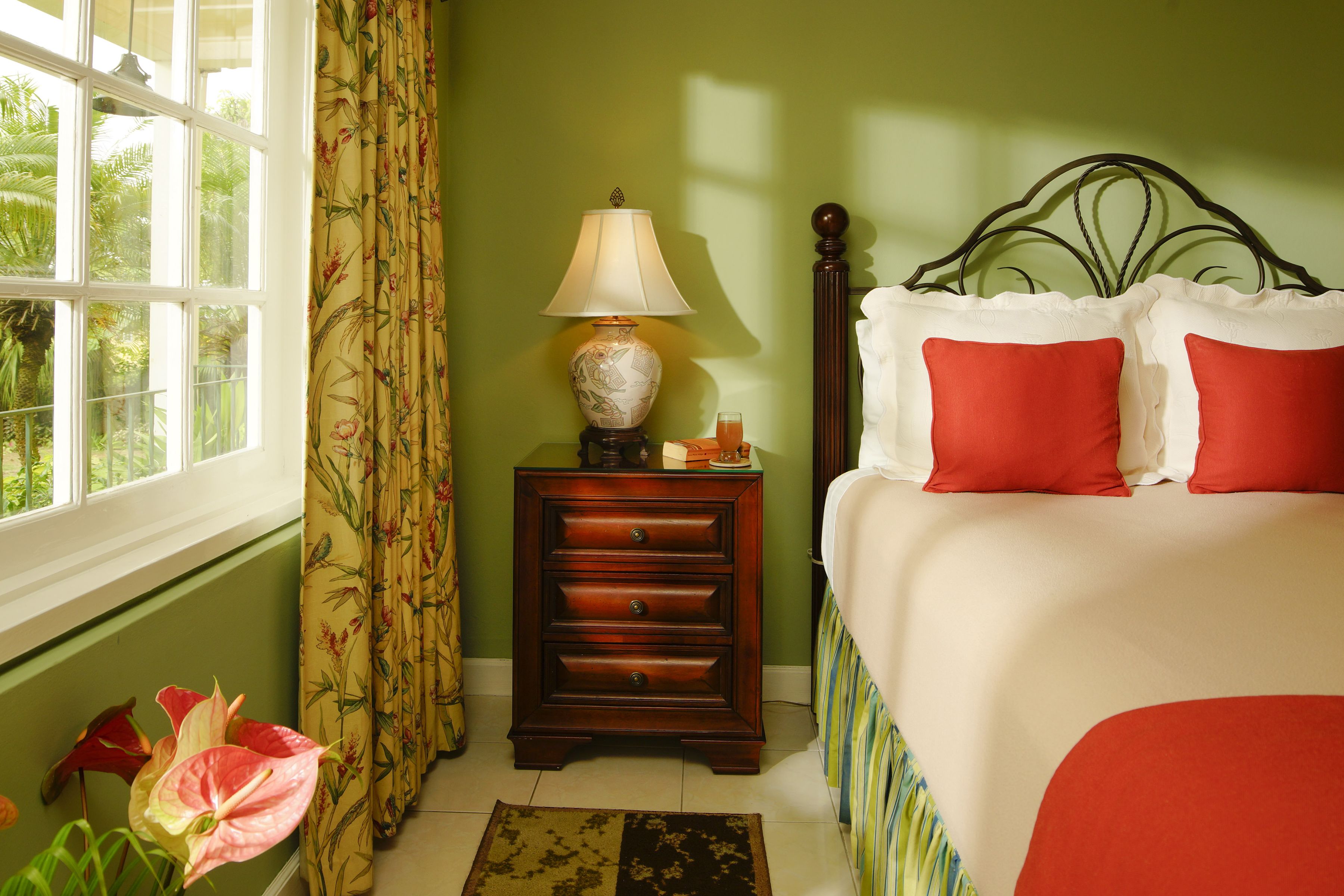 Una camera da letto con un letto, un comodino con una lampada, una finestra con tende e vista sul verde circostante.