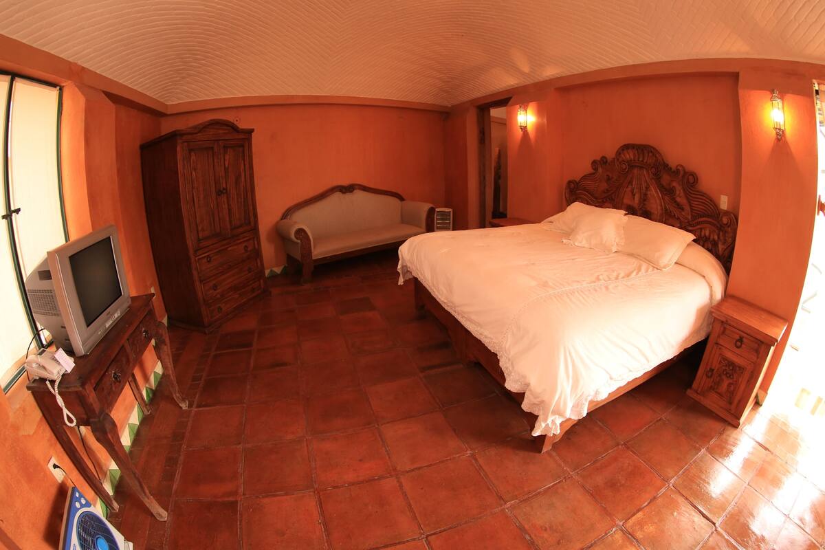 A bedroom with a bed, a wooden wardrobe, a television, and a radiator.