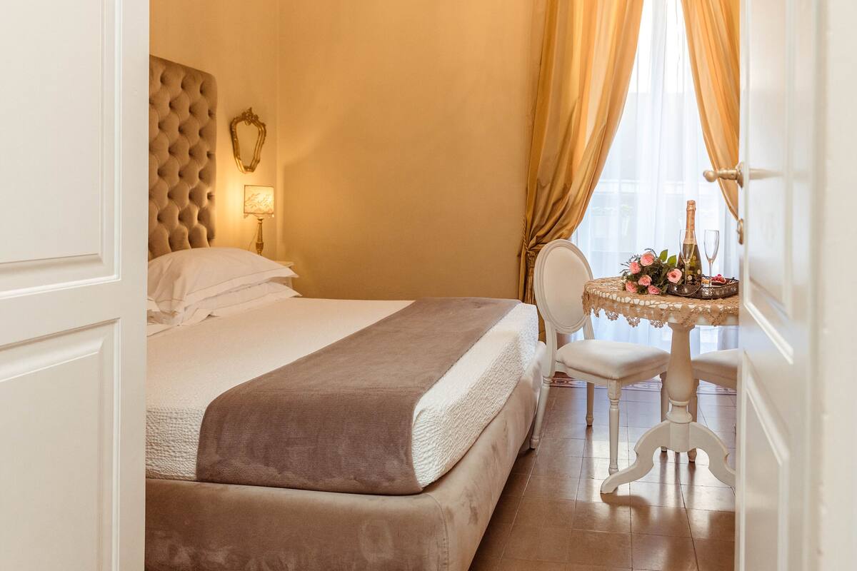 A hotel room with a large bed, a small table with a vase of flowers, and a chair.