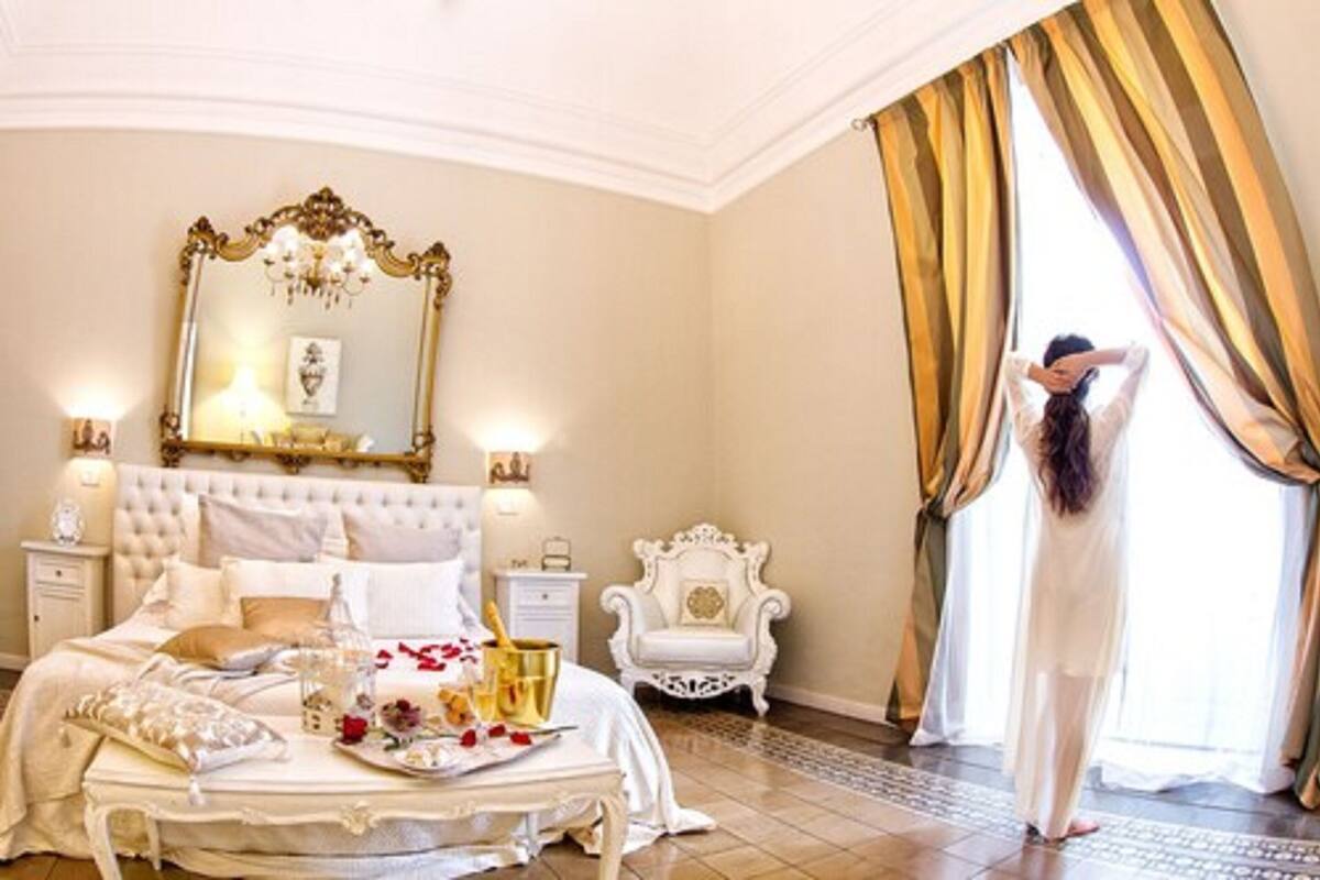 A luxurious bedroom with a large bed, a mirror, and a chandelier.