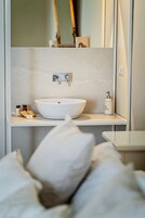 Un bagno con un lavandino bianco, uno specchio e articoli da toilette su uno scaffale.