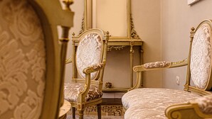 Una habitación con muebles ornamentados, que incluyen una cama y dos sillones, un espejo y suelo cubierto de alfombra.