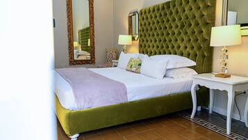Une chambre d’hôtel avec un lit recouvert d’un tissu vert, du linge de lit blanc, un grand miroir, deux lampes de chevet et une petite table de nuit blanche.