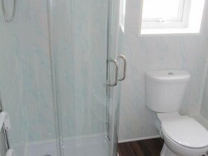 A bathroom with a toilet, a glass shower enclosure, and a window providing natural light. - Lindisfarne Holiday Flats (Blackpool)