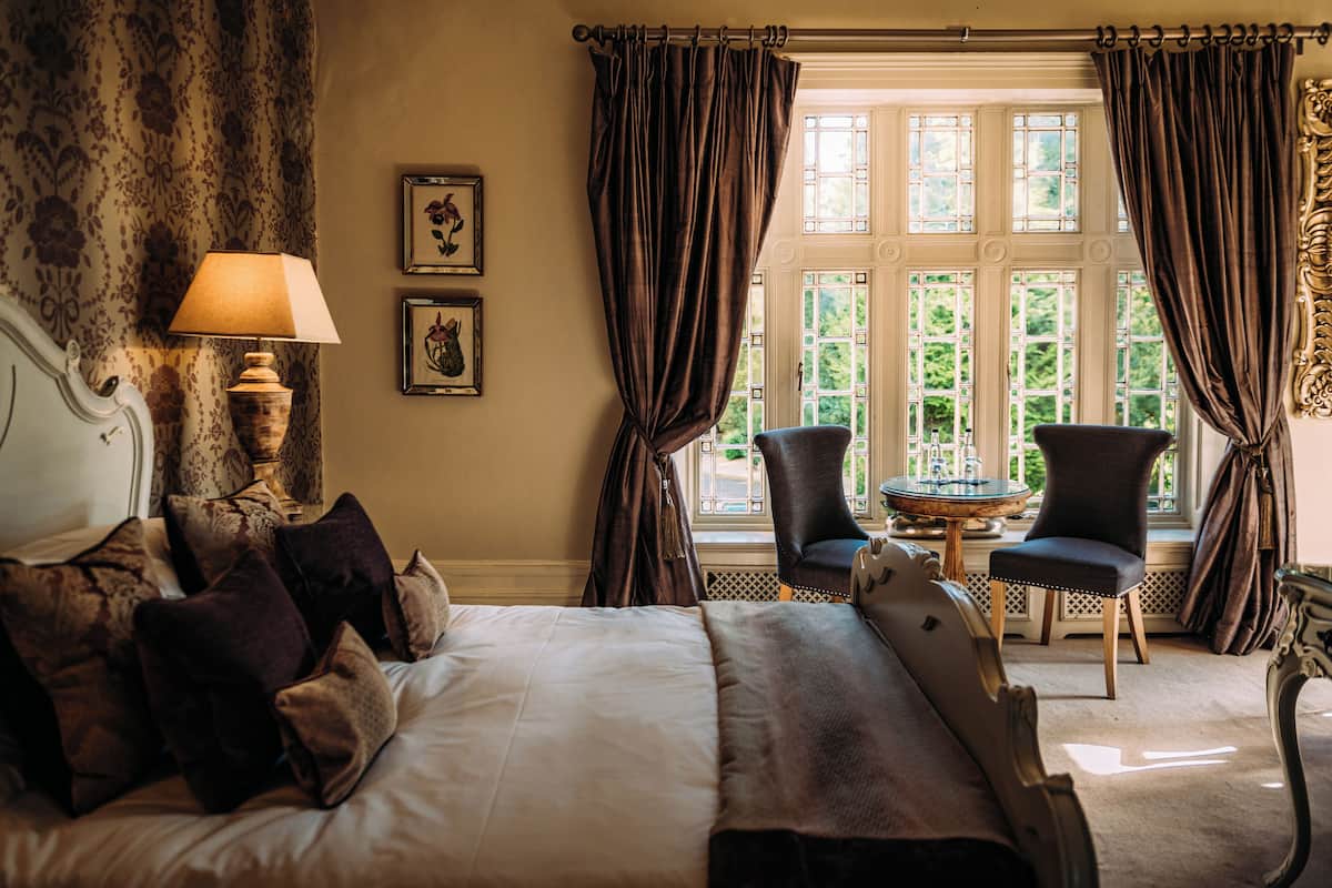 A hotel room with a large bed, a sitting area with a table and chairs, and a window with curtains.
