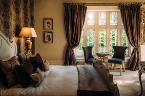 Ein Hotelzimmer mit einem großen Bett, einer Sitzecke mit Tisch und Stühlen sowie einem Fenster mit Vorhängen.