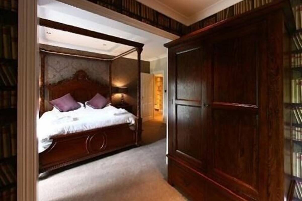 A bedroom with a four-poster bed, a large wooden wardrobe, and a carpeted floor.
