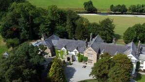 An aerial view of a large estate with multiple buildings, a well-maintained lawn, and a body of water in the background. - Mitton Hall Country House Hotel (Clitheroe)