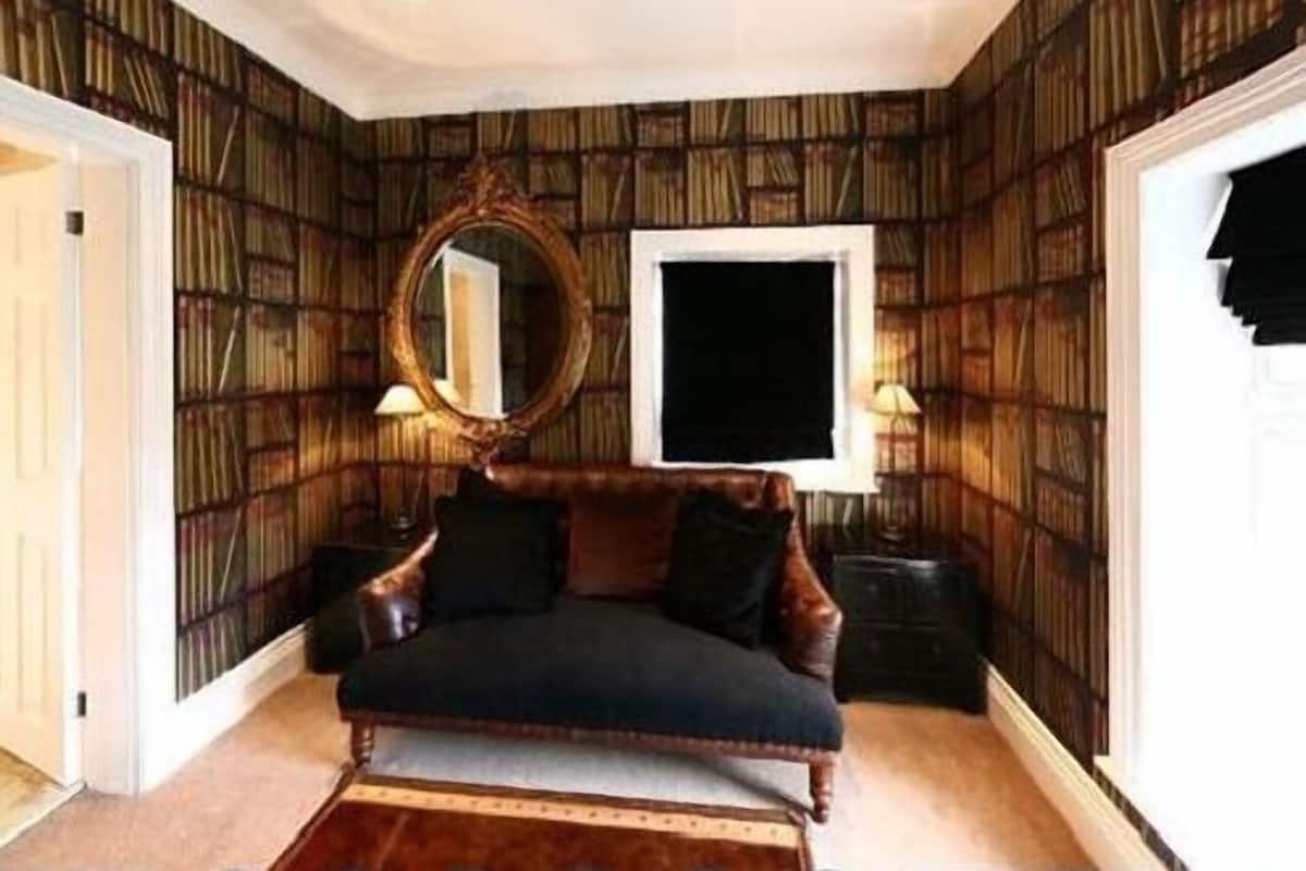 A room with a dark-colored sofa, a round mirror, and a window with a black frame.