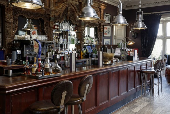 A bar area with a wooden counter, bar stools, and various bottles and glasses. - Mitton Hall Country House Hotel (Clitheroe)