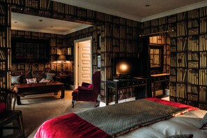 A room with a large bed, a red chair, a wooden desk, and bookshelves filled with books. - Mitton Hall Country House Hotel (Clitheroe)