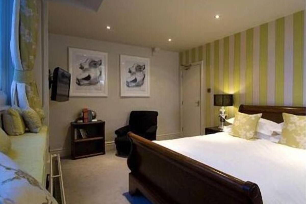 A hotel room with a large bed, a chair, a small table, and two framed pictures on the wall.