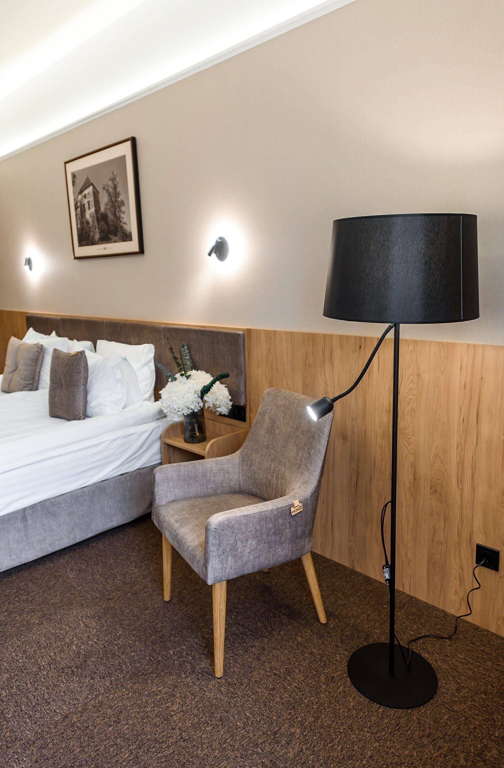 A hotel room with a bed, a chair, a lamp, and a picture on the wall.