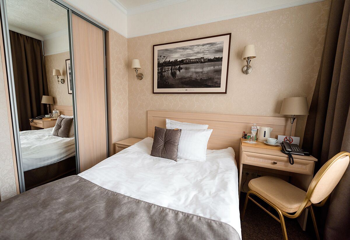 A hotel room with a bed, a desk, a chair, a mirror, and a framed picture on the wall.
