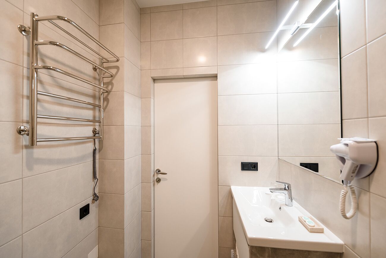 A modern bathroom with a glass shower enclosure, a towel rack, a sink with a mirror, and a hairdryer.