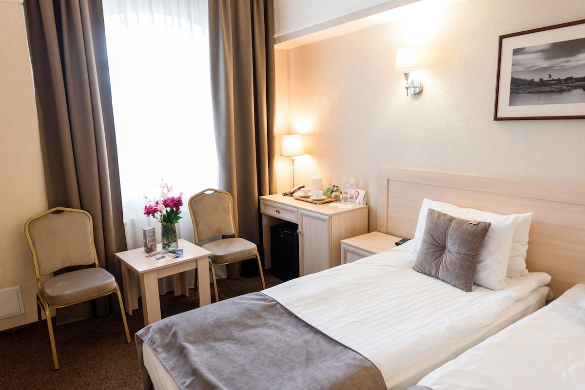 Ein Hotelzimmer mit Bett, Schreibtisch, Stuhl, Lampe und einer Vase mit Blumen.
