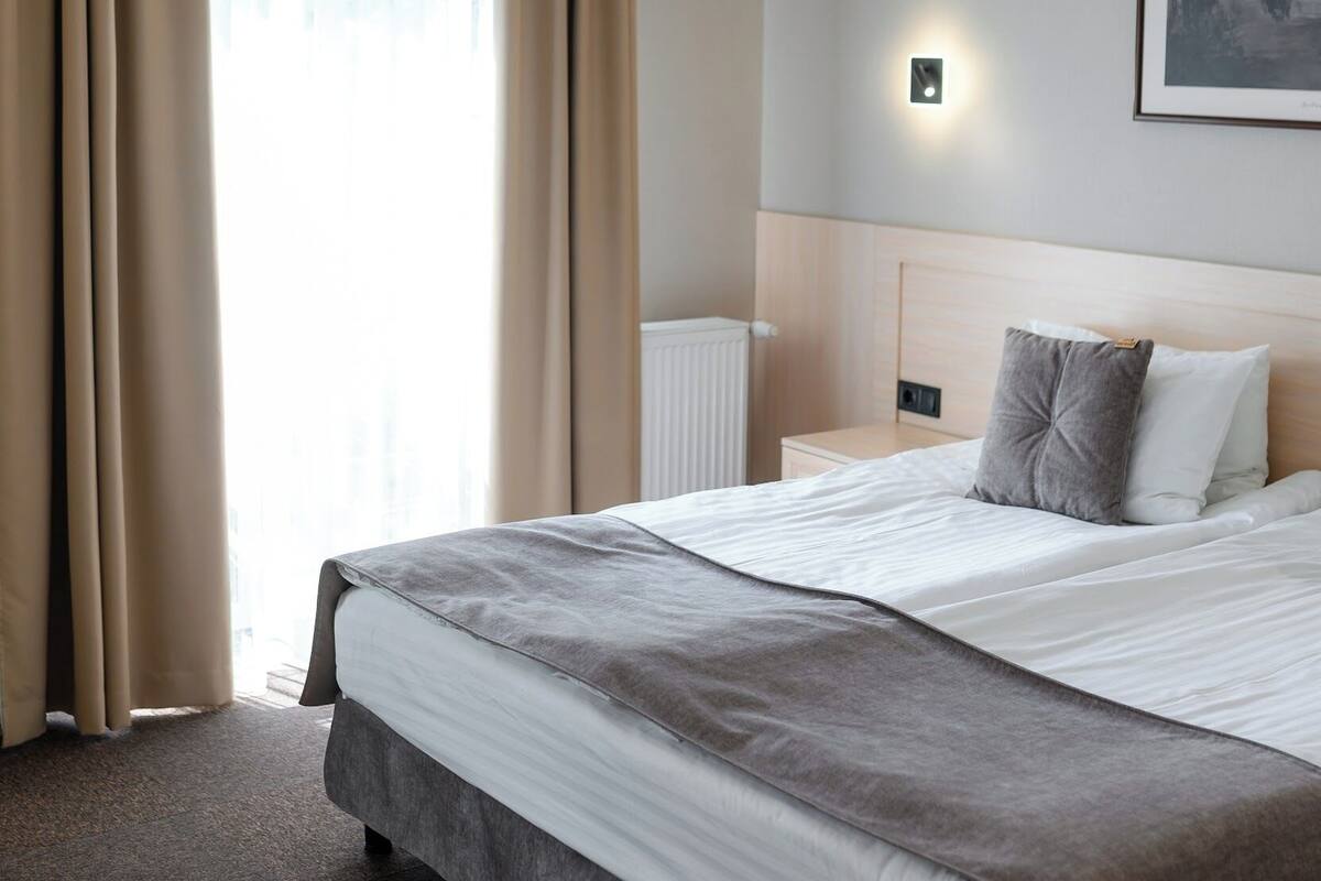 Ein Hotelzimmer mit einem großen Bett, beigen Vorhängen, einer Wandleuchte und einem gerahmten Bild an der Wand.