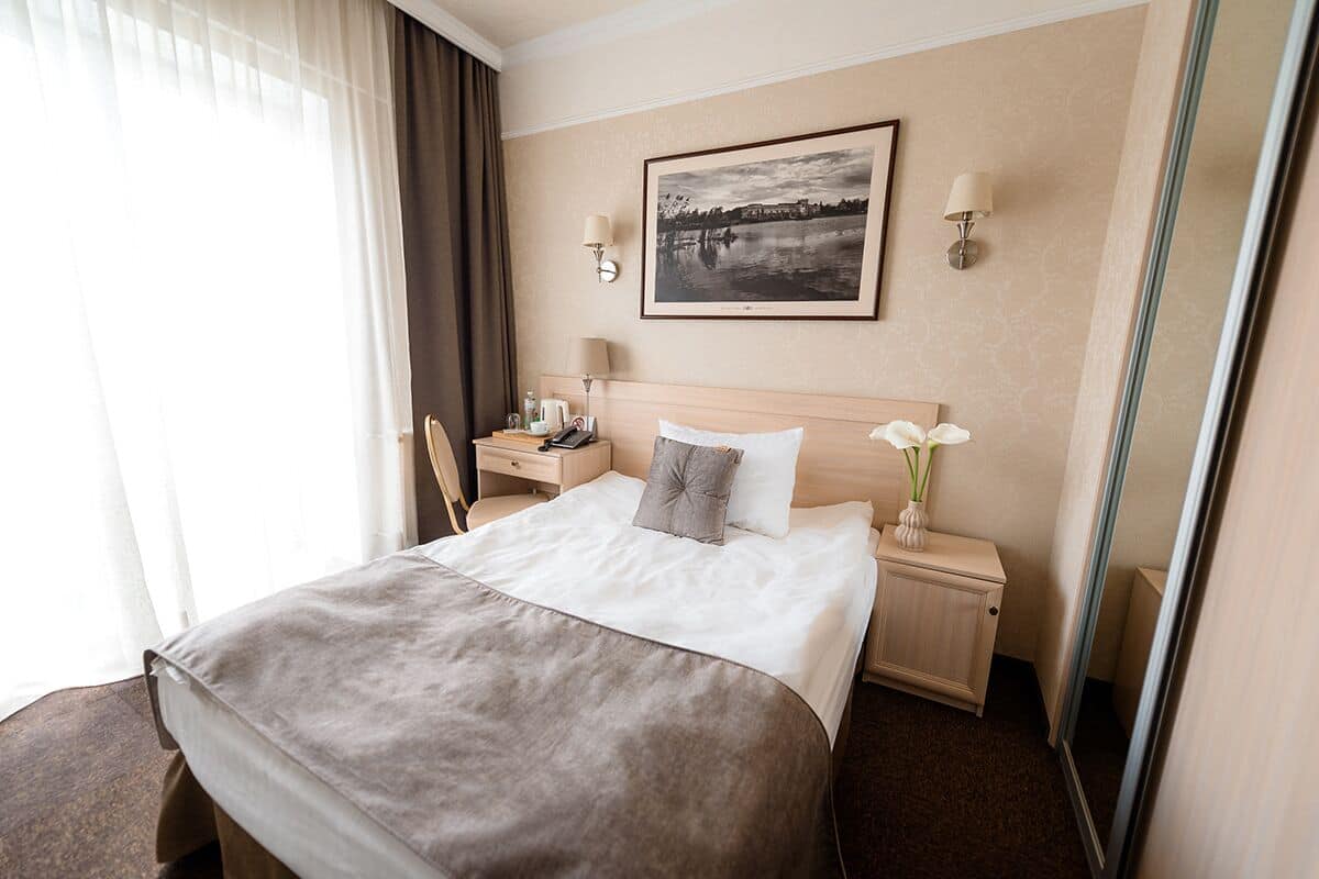 Ein Hotelzimmer mit einem großen Bett, einem Nachttisch mit Lampe, einem Sessel, einem Schminktisch und einem gerahmten Bild an der Wand.
