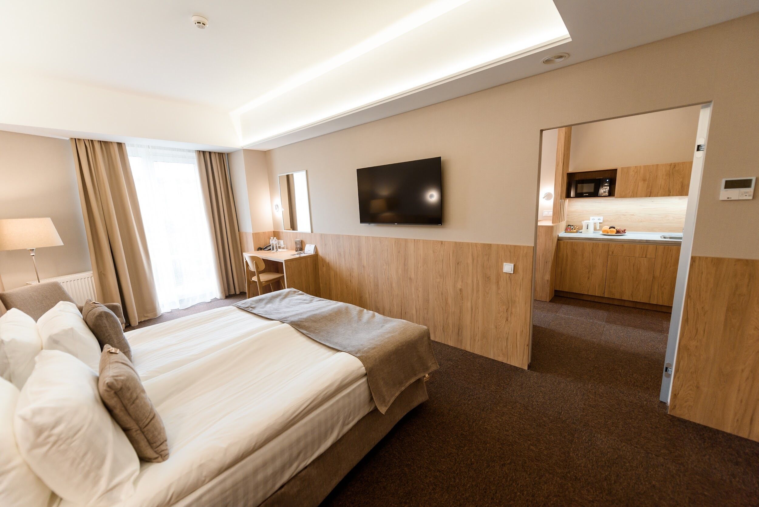 A hotel room with a large bed, a desk, a TV, and a kitchenette.
