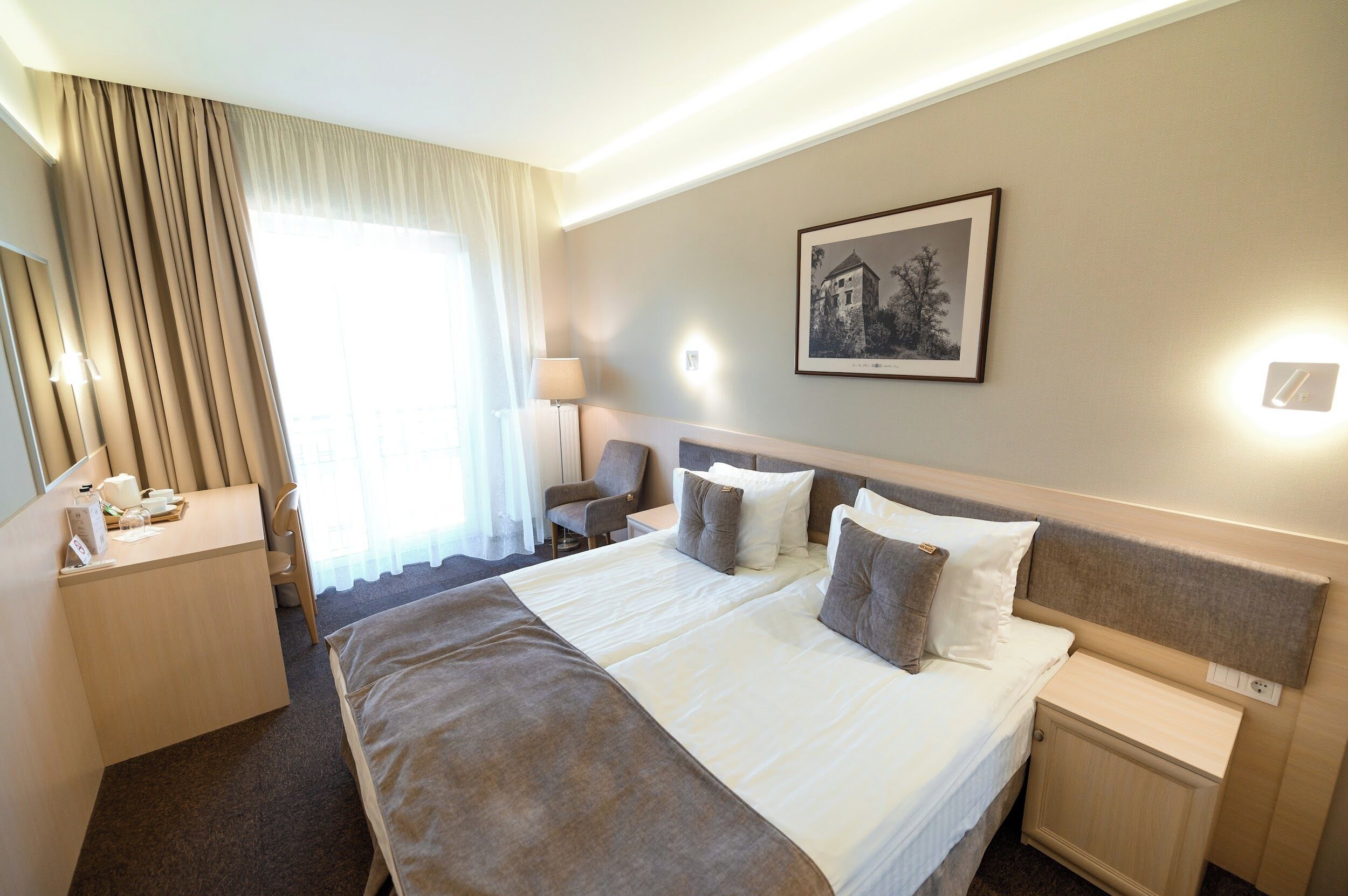 A hotel room with a large bed, a desk, a chair, and a nightstand.