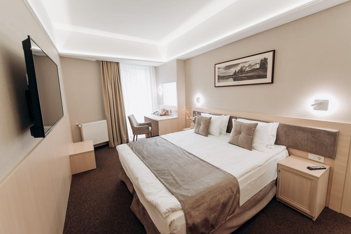 Ein Hotelzimmer mit einem großen Bett, einem Schreibtisch, einem Stuhl, einem Fernseher und einem gerahmten Bild an der Wand.