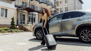 A person with a suitcase near a parked car in front of a multi-story building with balconies. - Nota Bene Hotel (Lviv)