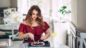A woman dining at a table with a wine glass, a small plate with food, and a vase with flowers. - Nota Bene Hotel (Lviv)